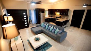A modern living room with a grey sofa, a white coffee table, and a blue rug. There is a kitchen area with dark cabinets and a microwave. - Stylish 3 Bedroom w/ Covered BBQ Area by the Pool (Sosúa)