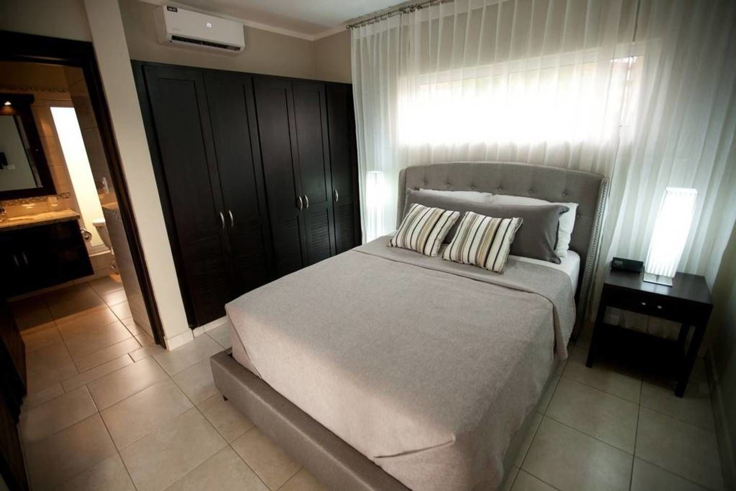 A bedroom with a bed, a nightstand, a wardrobe, and a bathroom visible through an open door.