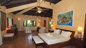 A spacious bedroom with a large bed, a sitting area with a chair and a small table, a television, and a painting on the wall. - Villa Las Palmas Caribbean Family Vacation Rental (Cabarete)