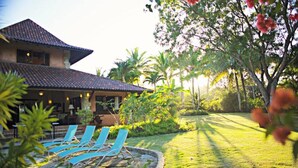 A house with a tiled roof, a swimming pool with blue lounge chairs, and a well-maintained lawn with palm trees. - Villa Las Palmas Caribbean Family Vacation Rental (Cabarete)