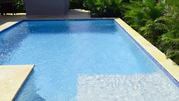 A rectangular swimming pool with clear blue water, surrounded by a tiled edge and lush greenery. - Ocean View 2 Bedroom Villa Newly Build in Gated Community (Sosúa)