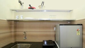 A compact kitchen with a stainless steel sink, a small refrigerator, and a microwave. There is a shelf above the sink with various kitchen items. - Noor Kitchenette Residency (Kanayannur)