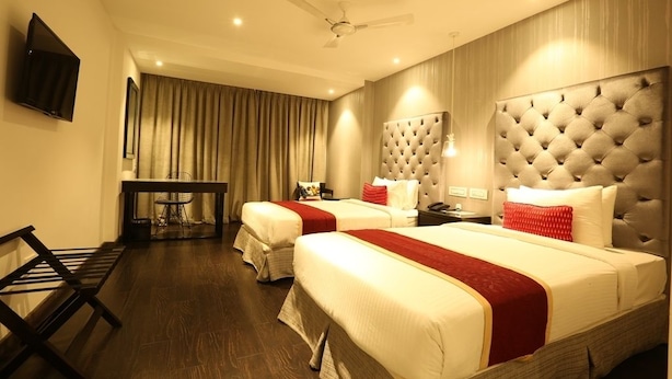A hotel room with two beds, a desk, a chair, a television, and a ceiling fan. - Noor Kitchenette Residency (Kanayannur)