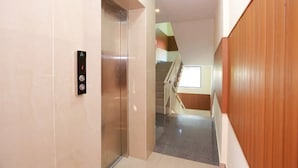 A hallway with a modern elevator, a staircase, and a view of a room with a window. - Noor Kitchenette Residency (Kanayannur)