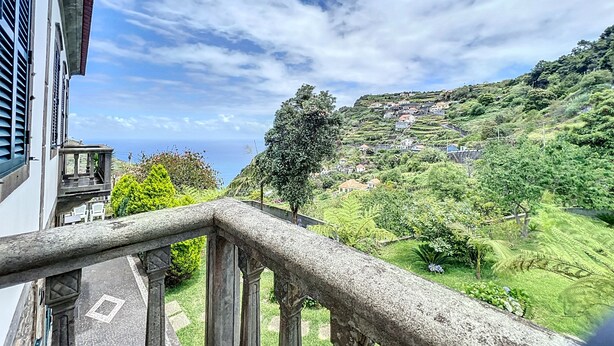 A balcony with a stone balustrade overlooking a hillside with houses and greenery. - Quinta do Serrado II (Porto Moniz)