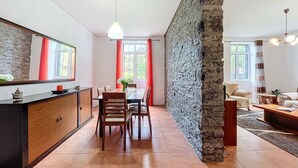 A modern living room with a dining area, stone accent wall, and large windows. - Quinta do Serrado II (Porto Moniz)