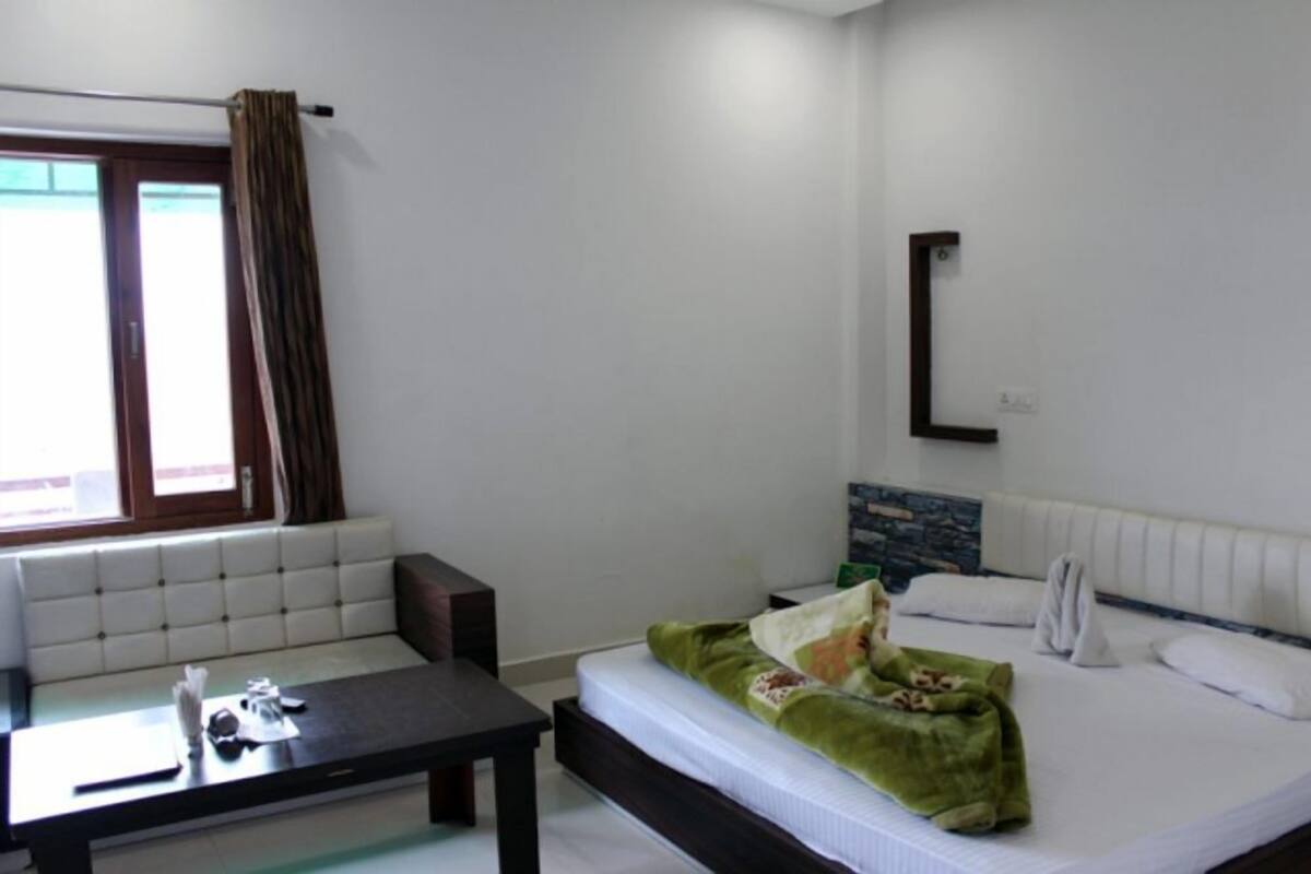 Ein Hotelzimmer mit Bett, kleinem Tisch, einer Couch, einem Fenster mit Vorhängen und einem wandmontierten Spiegel.