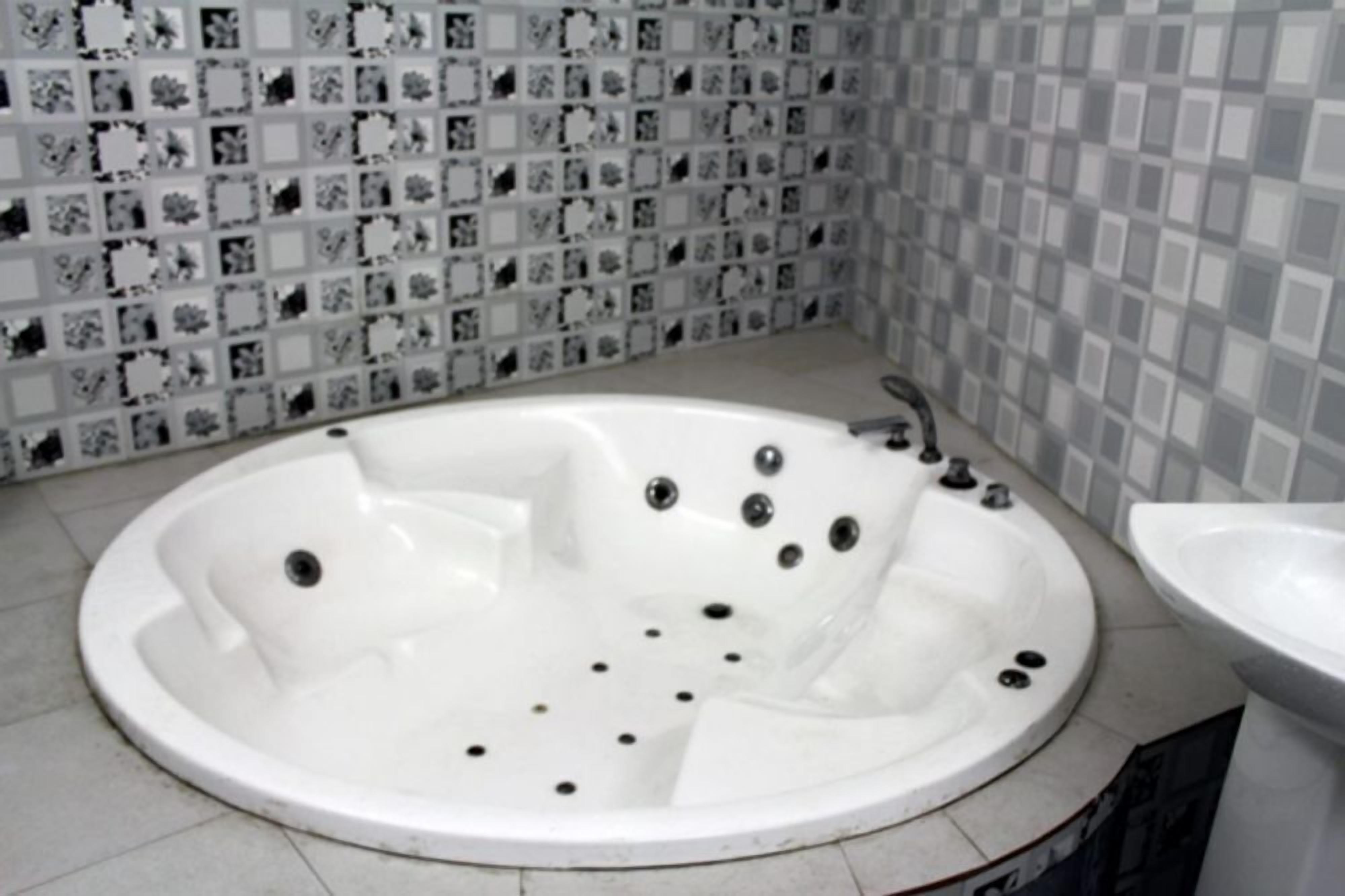 Ein Badezimmer mit einer großen weißen Badewanne, einem Waschbecken und einer gefliesten Wand mit einem sich wiederholenden Muster.