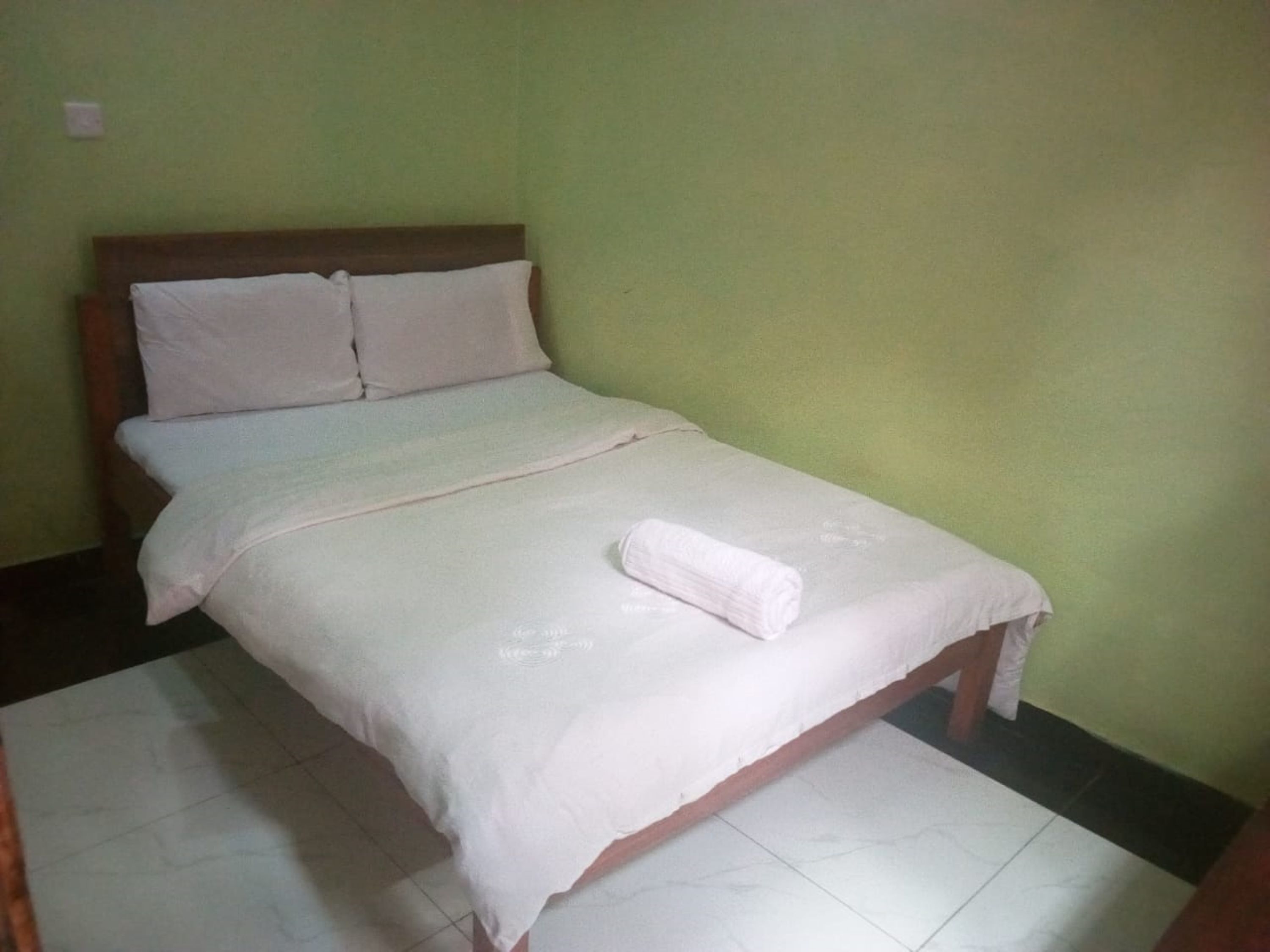 A single bed with a wooden headboard, a white bedspread, and a folded white towel on the footboard.