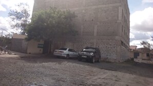 Un edificio de fachada de ladrillo, un árbol en primer plano y dos coches estacionados.