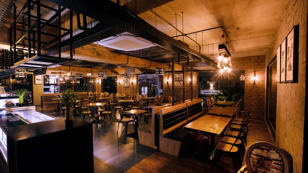 Un restaurant amb taules i bancs de fusta, parets de maó al descobert i lluminàries penjants.