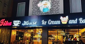 Una cafetería con un letrero de neón e una gran ilustración de helado y pastel.