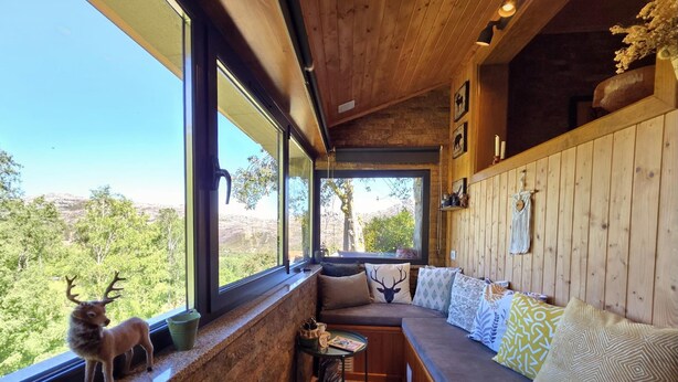 A cabin with a wooden interior, large windows, a built-in bench, and a view of the outdoors.