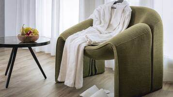 A room with a green armchair, a white bathrobe, a bowl of fruit, and a pair of slippers on the floor.