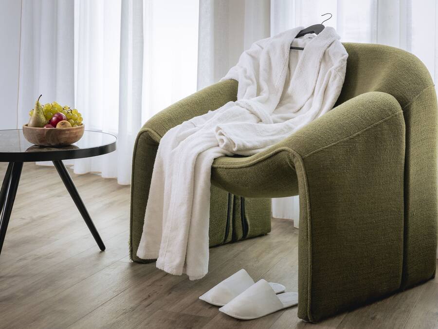 Ein Zimmer mit einem grünen Sessel, einem weißen Bademantel, einer Obstschale und Hausschuhen auf dem Boden.