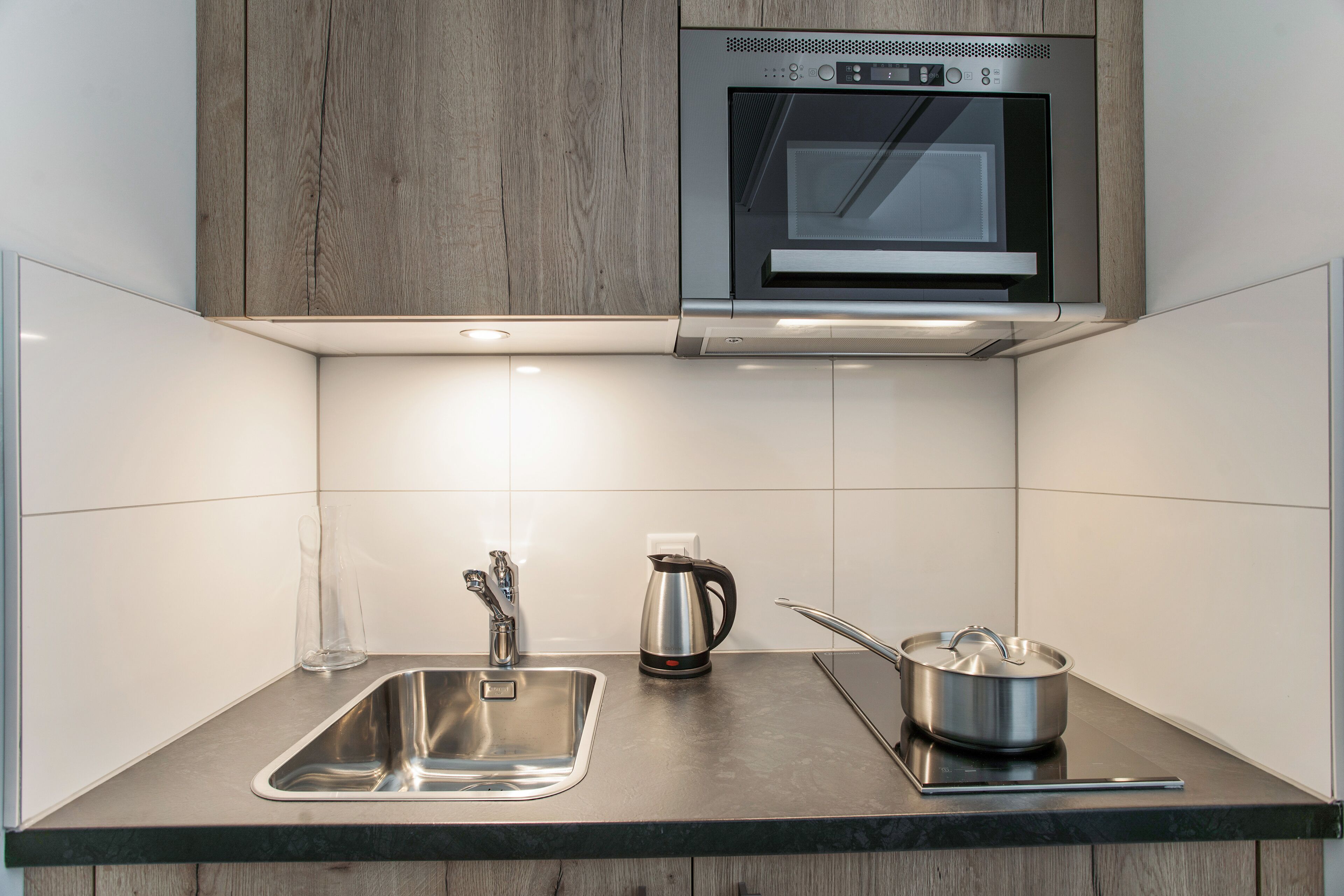 A modern kitchen with a stainless steel sink, a kettle, and a pot on the counter.
