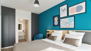 A modern hotel room with a large bed, a desk, and a chair. There are framed pictures on the wall and a bathroom visible through an open door. - Appart'City Collection Genève Aéroport Vernier (Vernier)