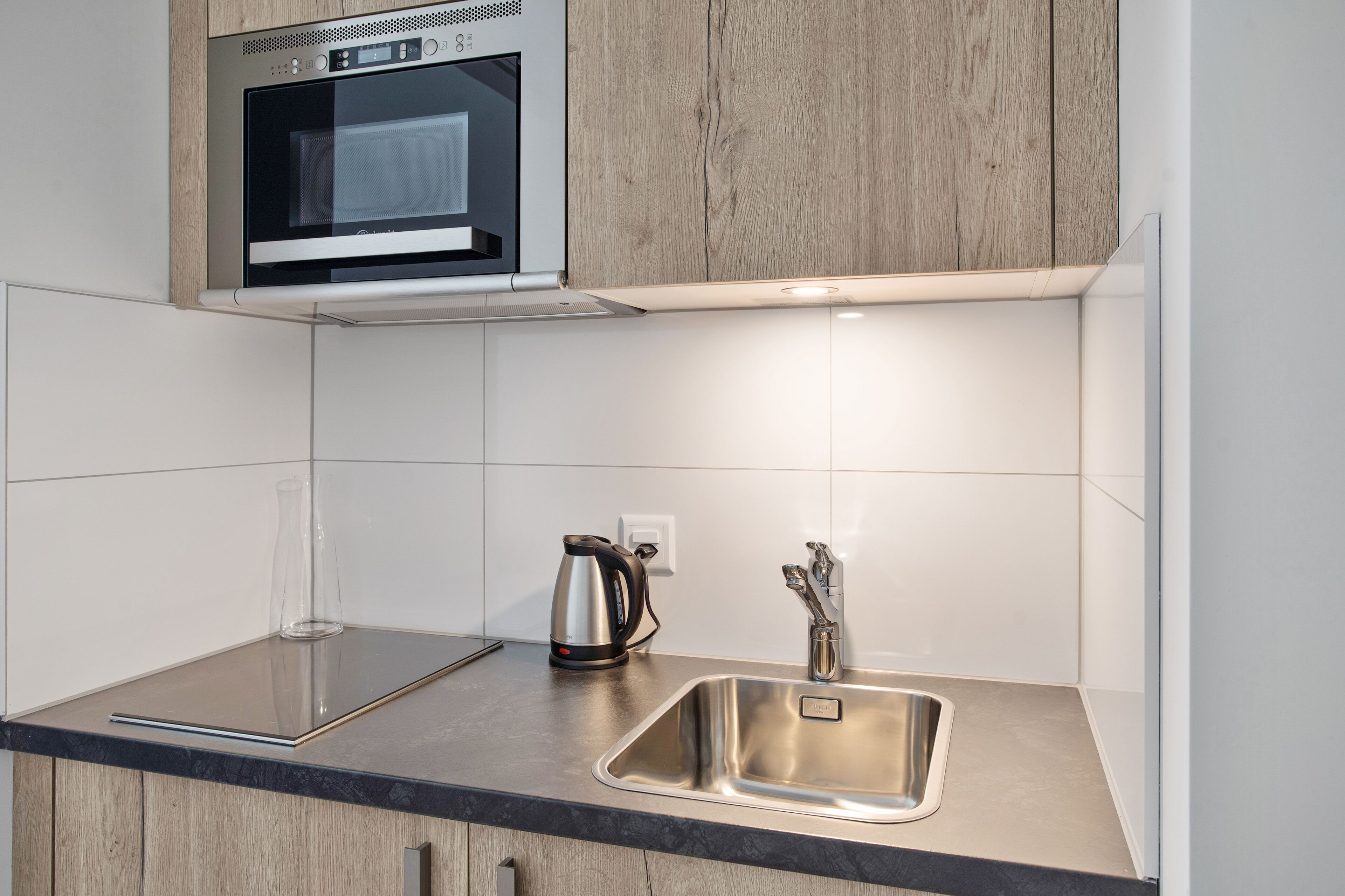 A modern kitchen with a built-in microwave, a stainless steel sink, and a kettle on the countertop.
