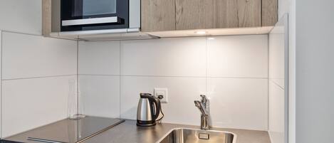 A modern kitchen with a built-in microwave, a stainless steel sink, and a kettle on the countertop.