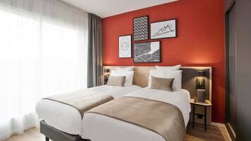 Una habitación de hotel con dos camas, una pared de acento roja y obras de arte enmarcadas.