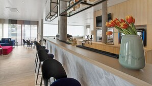 A modern bar area with a marble countertop, black bar stools, and a vase of tulips. - Appart'City Collection Genève Aéroport Vernier (Vernier)