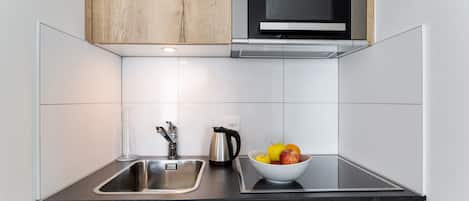 Cocina moderna con un lavamanos de acero inoxidable, una tetera y un bol de fruta sobre la encimera.