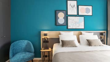 Habitación de hotel moderna con paredes verde azulado, una cama grande, un sillón azul y cuadros en la pared.