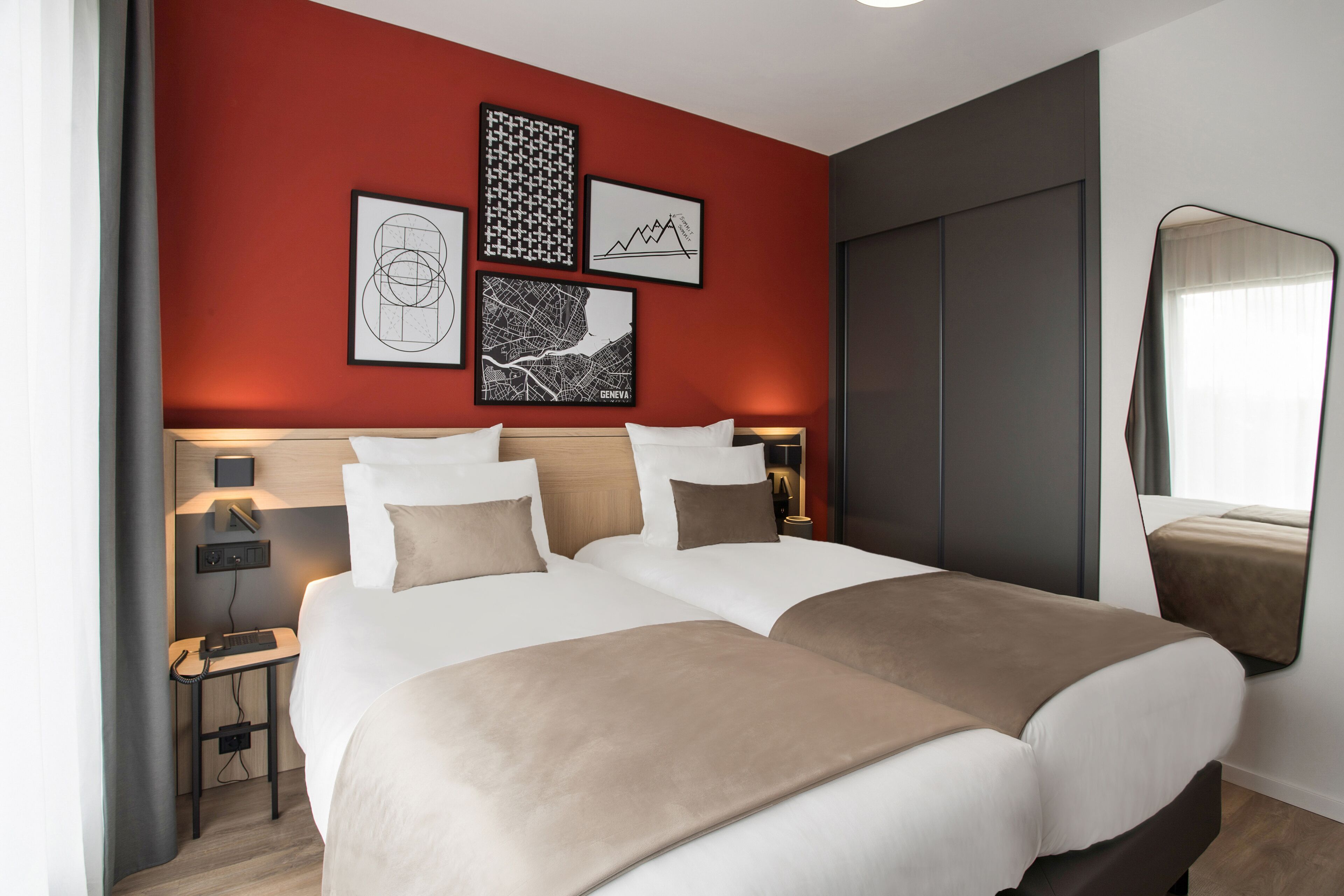 Cama de casal com duas almofadas, mesa de cabeceira com abajur e parede com quadros.