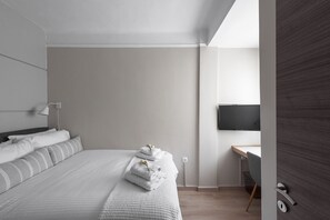 Ein modernes Hotelzimmer mit einem ordentlich bezogenen Bett, einem Schreibtisch mit Stuhl und einem wandmontierten Flachbildfernseher.