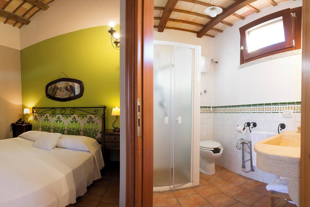 Een slaapkamer met een groene wand, een bed met wit beddengoed, een nachtkastje met een lamp en een ingelijst kunstwerk boven het bed.