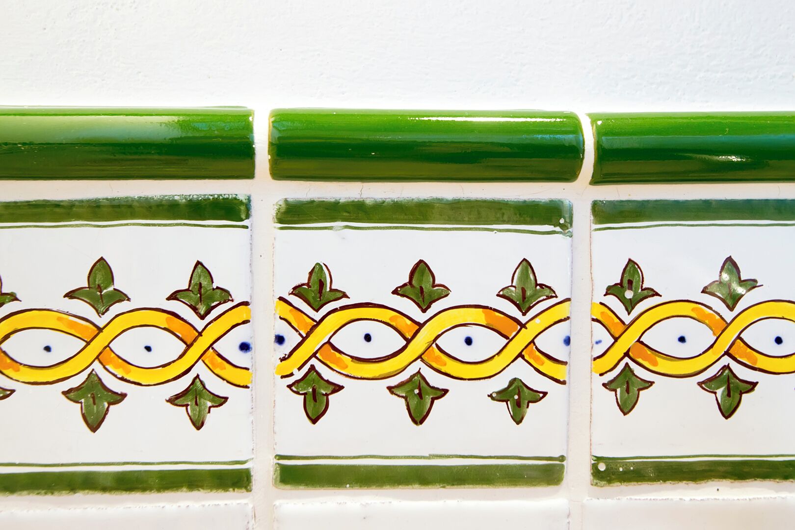 Pared de azulejos con un diseño repetido en tonos verde, amarillo y blanco.