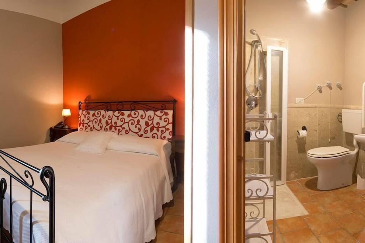 Een slaapkamer met een bed, nachtkastje en een badkamer met douche, toilet en wastafel.