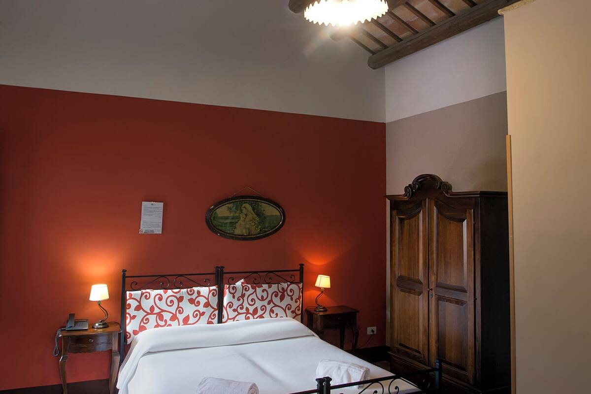 Een slaapkamer met een houten plafond, een bed met metalen frame, twee nachtkastjes met lampen en een kledingkast.