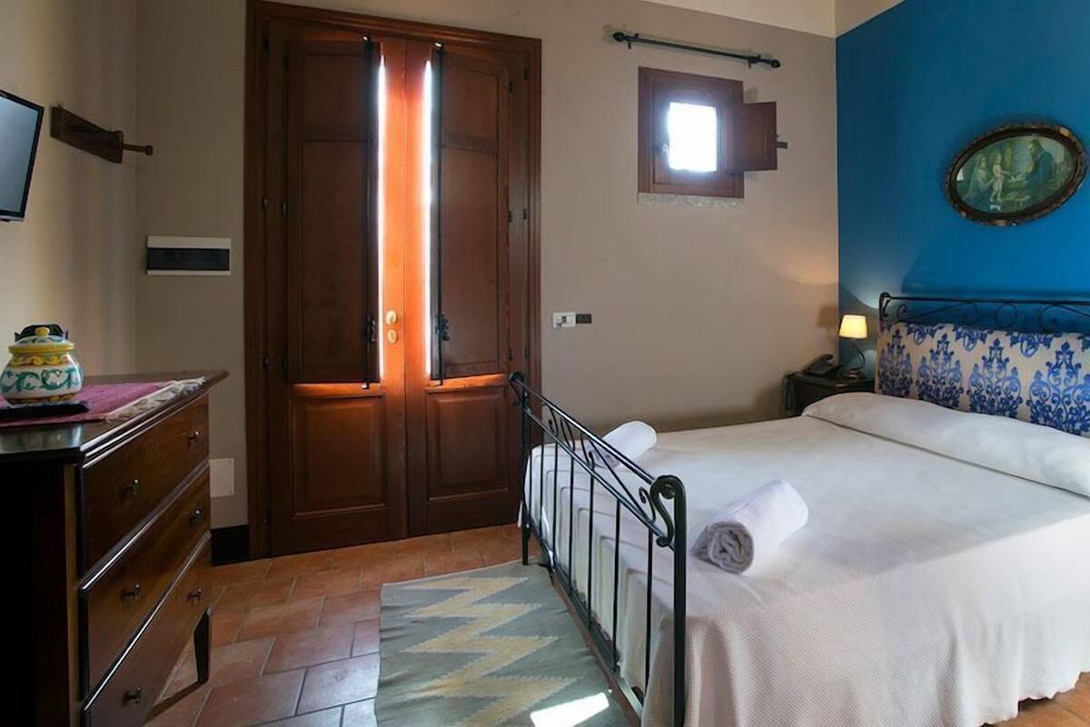 Een slaapkamer met een bed, een kaptafel, een houten deur, een raam en een blauwe muur met een schilderij.