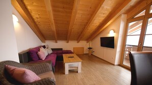 Une pièce confortable de style loft, avec un plafond en bois, un canapé, une table basse et un téléviseur fixé au mur.