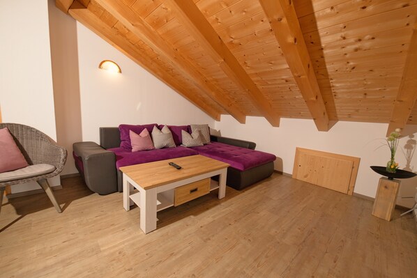 Une pièce chaleureuse avec un plafond en bois, un canapé avec des coussins, une petite table et une chaise.
