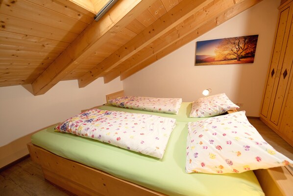 Un dormitorio con techo inclinado, vigas de madera, una cama con ropa de cama floral, una mesita de noche y una lámpara de pared.