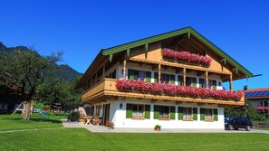 Traditional Alpine-style building with a balcony and green trim, set amidst a well-maintained lawn and playground.
