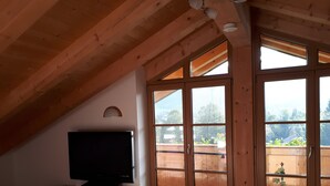 Une pièce avec un plafond en pente, un téléviseur posé sur un meuble en bois et de grandes portes-fenêtres coulissantes donnant sur un balcon extérieur.