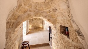 A narrow stone passageway leading to a room with a tiled floor and a small stool.