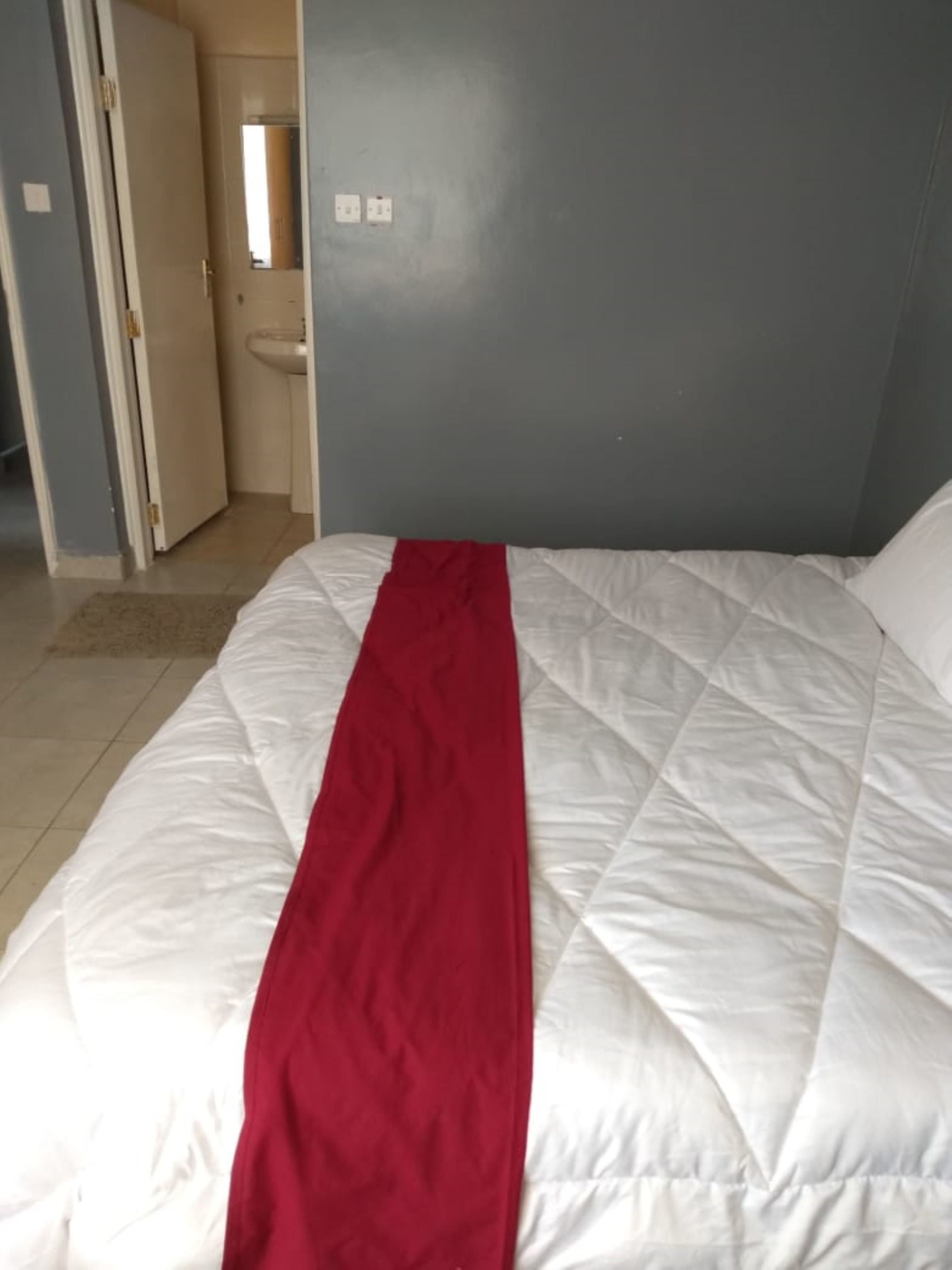 A bed with a white and red bedspread in a room with a blue wall and a white door.