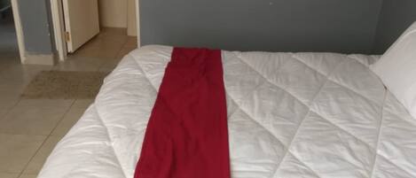 A bed with a white and red bedspread in a room with a blue wall and a white door.