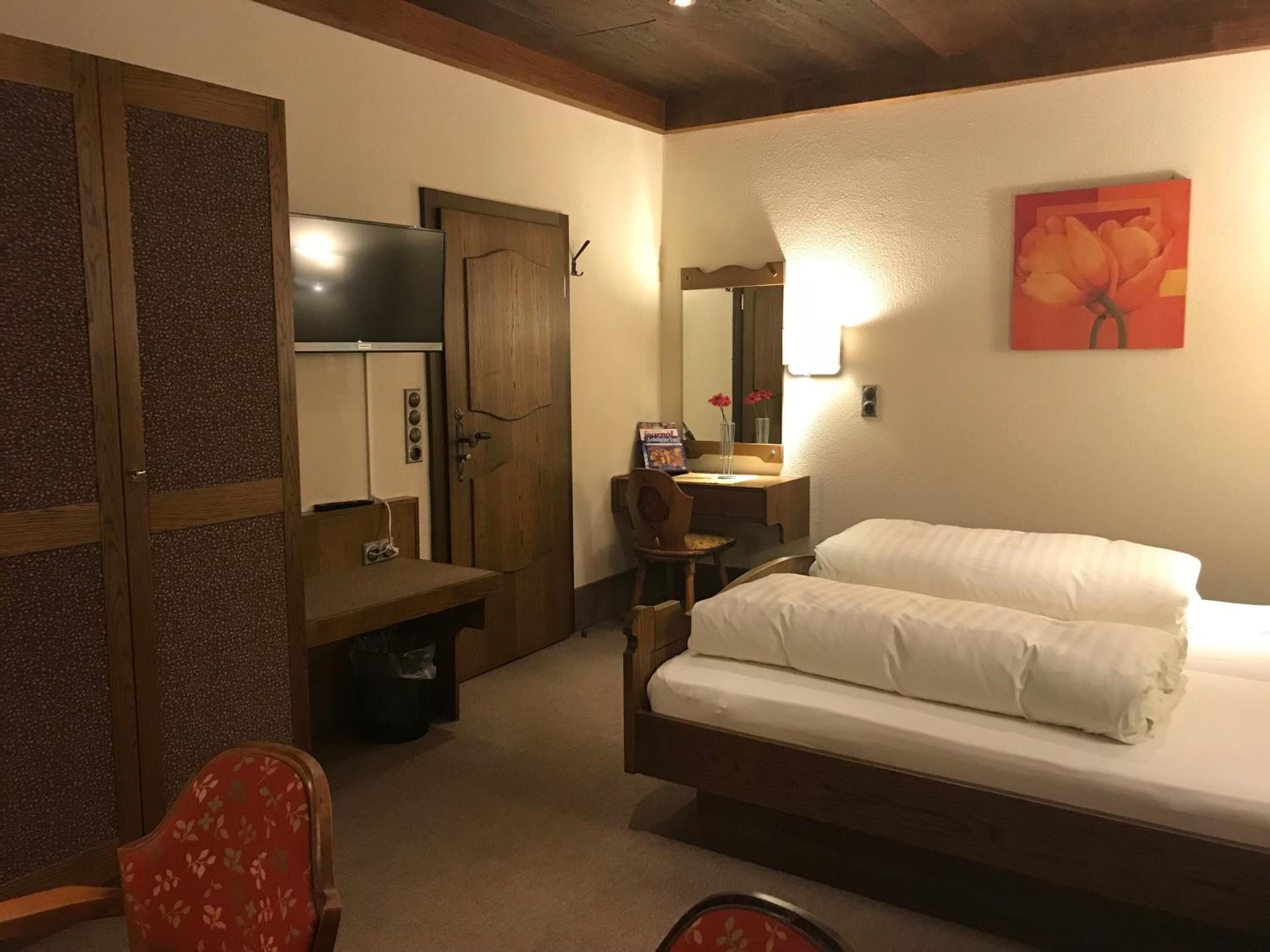 Habitación de hotel con cama, escritorio, silla, televisor y un cuadro en la pared.