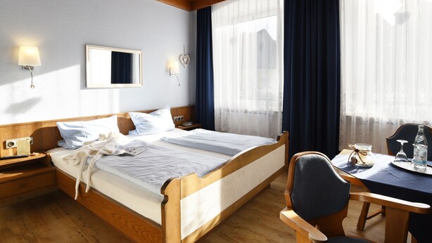 Une chambre d’hôtel avec un lit en bois, des tables de chevet, un bureau avec une chaise et une fenêtre avec des rideaux.
