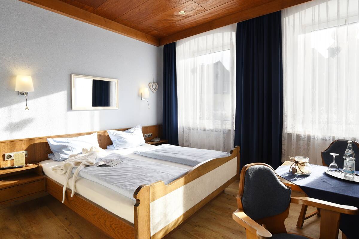 Ein Hotelzimmer mit einem hölzernen Bett, Nachttischen, einem Schreibtisch mit Stuhl und einem Fenster mit Vorhängen.