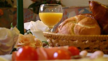 A breakfast setting with a glass of orange juice, a basket of bread, and some tomatoes.