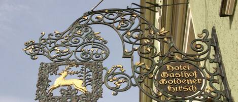 Un letrero de metal con el emblema de un ciervo y el texto "Hotel Gasthof Goldener Hirsch".