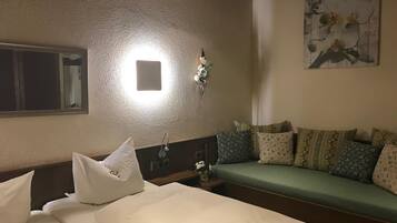 A hotel room with a bed, a sofa, a wall-mounted light, a mirror, and a painting.