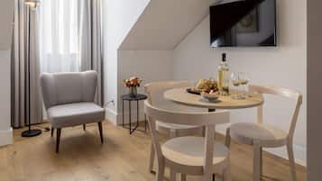 A modern living room with a grey sofa, a round wooden dining table, and a flat-screen TV mounted on the wall.