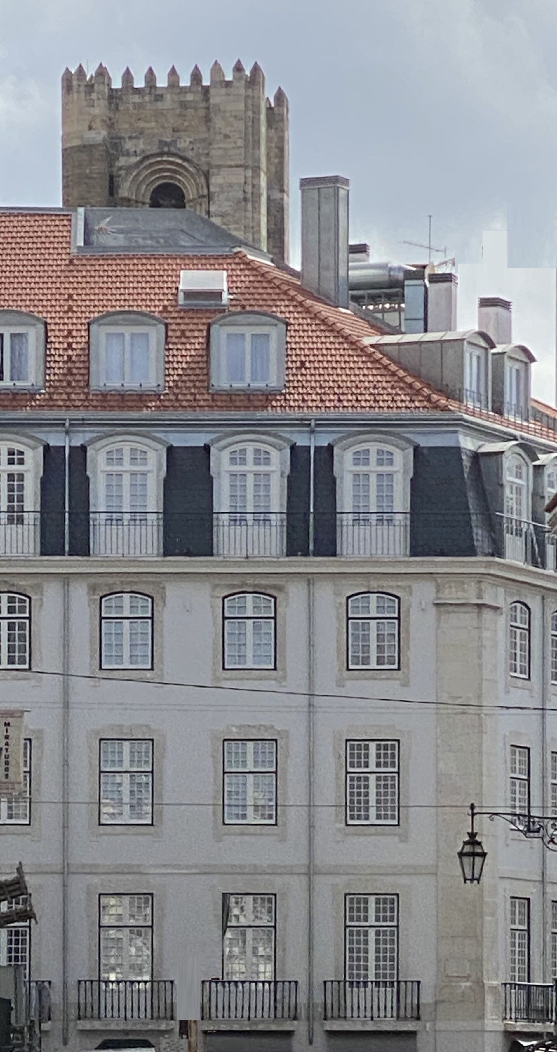 Um edifício histórico com torre em turretes, várias janelas e telhado de telhas vermelhas.